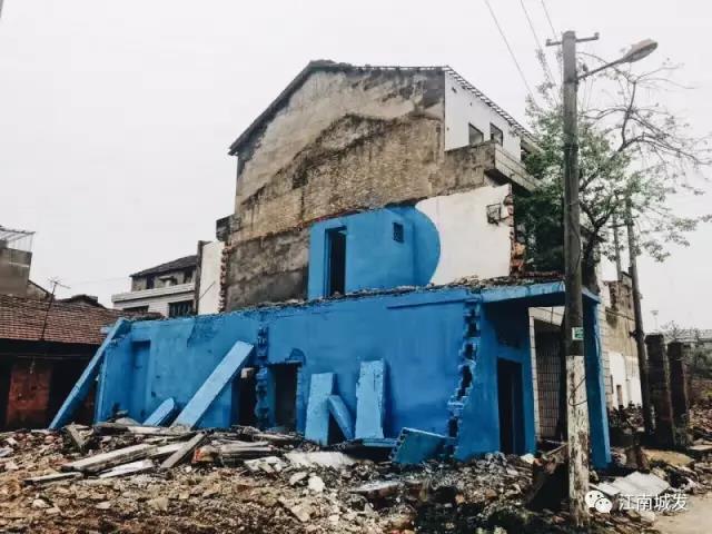 △ 這棟建筑是臨江最近的半拆遷建筑物的遺留，沅江和堤壩成為了展覽的天然背景。創(chuàng  )作團隊對這棟建筑進(jìn)行了半涂裝，將符號性的沅水曲線(xiàn)與拆遷進(jìn)行中的建筑立面進(jìn)行意義的疊造，它們共同觸發(fā)了場(chǎng)所空間多元語(yǔ)境的生成，把拆遷這種暫時(shí)破壞性、干擾性的介入行動(dòng)與沅水右岸發(fā)展的未來(lái)性、美好性緊密融合。
